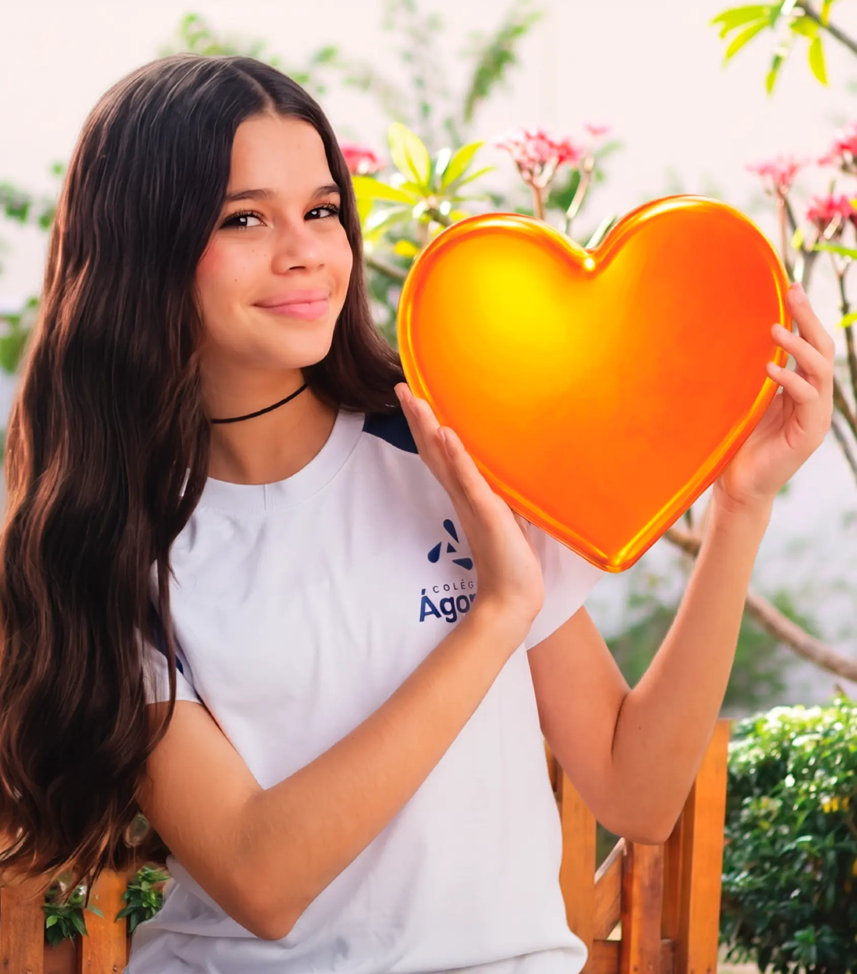 Aluna do Colégio Ágape sorrindo e segurando um coração laranja